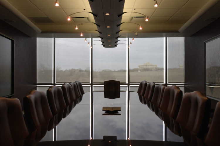 a boardroom with a shiny granite conference table in the middle and dim lights above