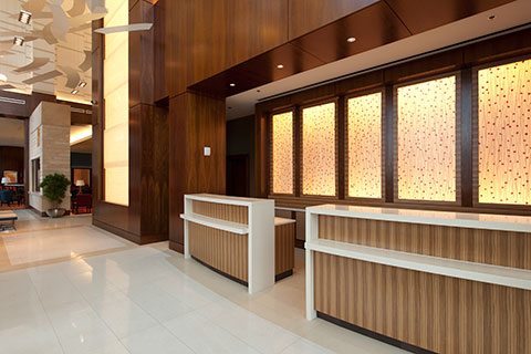 A modern hotel lobby with wood paneled walls, two reception desks, and glowing light panels.