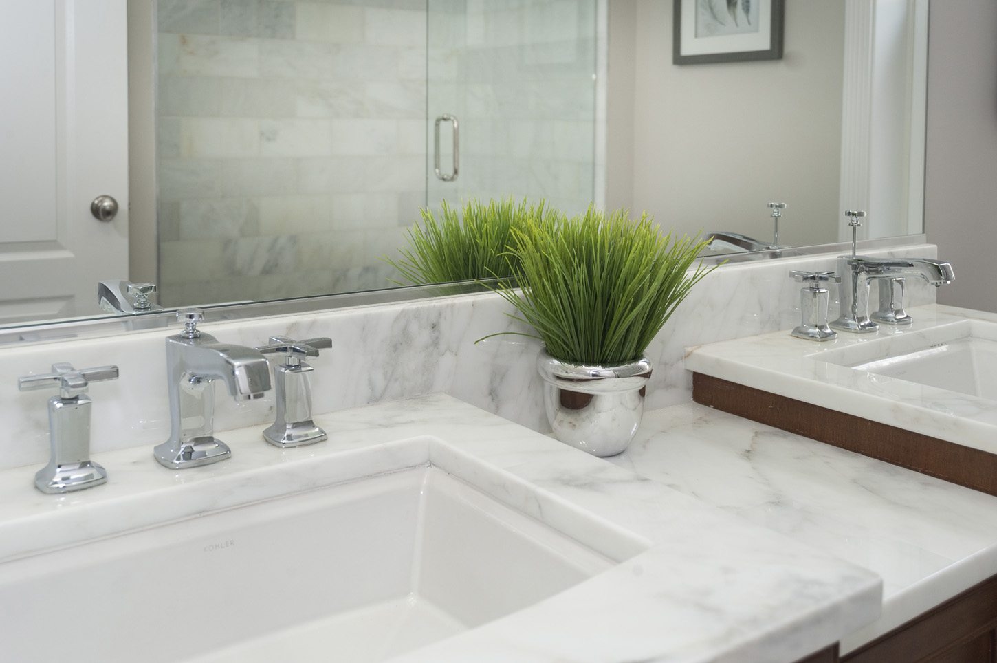 A double vanity with marble countertops, chrome faucets, and a plant in a silver pot.