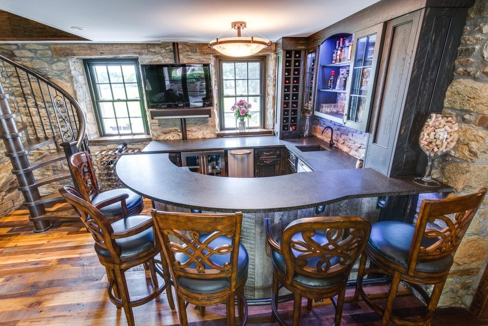 A rustic basement bar with stone walls, a dark curved counter, and a spiral staircase