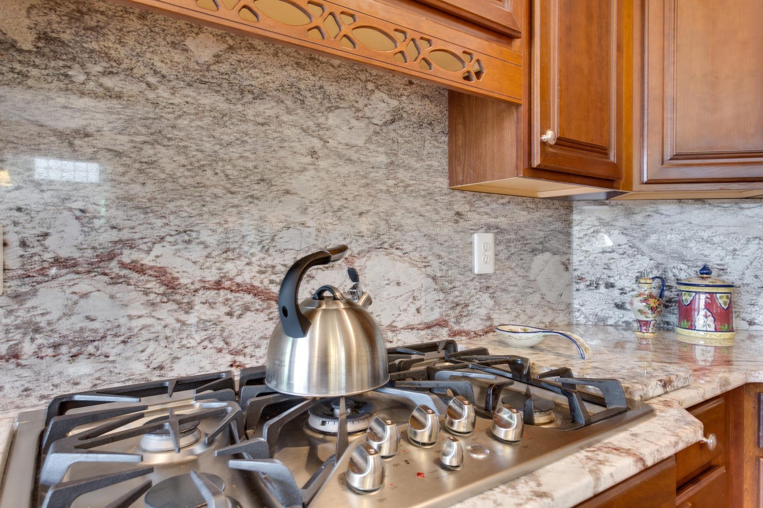 A kitchen with wood cabinets, a gas cooktop, and a reddish-brown veined stone backsplash.